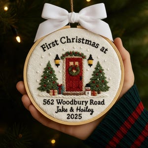 May include: Embroidered Christmas ornament in a wooden hoop. The design features a red door with a wreath, Christmas trees, and the text "First Christmas at 562 Woodbury Road Jake & Hailey 2025". A white bow is at the top.