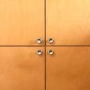 Puede incluir: Cuatro puertas de armario de madera de tono claro dispuestas en cuadr&iacute;cula. Cada puerta cuenta con un peque&ntilde;o pomo circular de metal plateado pulido situado cerca del punto de uni&oacute;n central de las cuatro puertas.