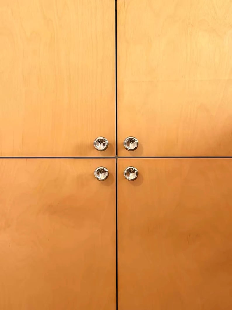 Puede incluir: Cuatro puertas de armario de madera de tono claro dispuestas en cuadr&iacute;cula. Cada puerta cuenta con un peque&ntilde;o pomo circular de metal plateado pulido situado cerca del punto de uni&oacute;n central de las cuatro puertas.