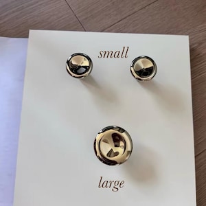 May include: A white square display board featuring three polished silver-tone circular knobs. Two smaller knobs are positioned near the top with the text small printed between them, and one larger knob is centered below with the text large printed below it.