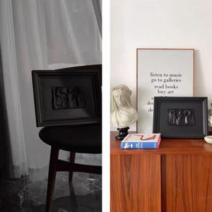 K&ouml;nnte beinhalten: Zwei schwarz gerahmte Reliefskulpturen, eine auf einem Stuhl und eine auf einem Holzschrank. Die Skulpturen zeigen Figuren im klassischen Stil. Ein gerahmter Druck mit Text und eine B&uuml;ste sind ebenfalls zu sehen.