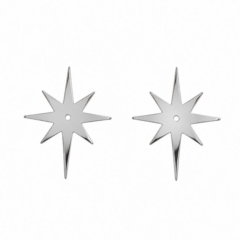May include: A pair of silver-toned metal earring jackets shaped like eight-pointed stars. Each star features a central circular hole designed to accommodate an earring post, with elongated, sharp points radiating from the center.