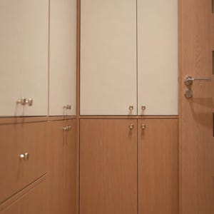 Puede incluir: Una unidad de almacenamiento de suelo a techo con armarios y cajones de madera clara, combinados con puertas superiores de color blanco roto. La unidad incluye peque&ntilde;os pomos de metal plateado y una puerta de madera a juego con manilla.