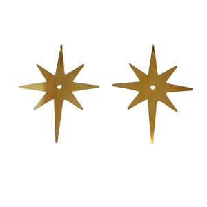 May include: Two identical gold-colored metal star ornaments, each featuring eight points of varying lengths and a small circular hole centered in the middle. The stars have a smooth, reflective surface and a flat, symmetrical design.