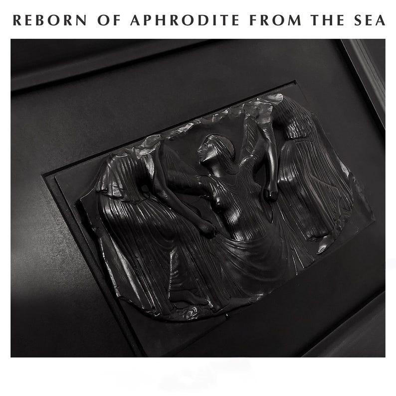 K&ouml;nnte beinhalten: Schwarze Reliefskulptur mit drei Figuren in flie&szlig;enden Gew&auml;ndern und dem Text "REBORN OF APHRODITE FROM THE SEA" oben. Die mittlere Figur hebt die Arme. Die Skulptur ist in einen dunklen Rahmen gesetzt, was einen dramatischen Kontrast erzeugt.