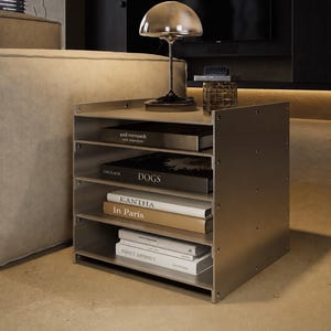 May include: A metallic, four-shelf storage unit with exposed side screws, holding books titled Axel Vervoordt, DOGS, KANTHA, In Paris, and Perfect Imperfect. A dome-shaped lamp sits on the top surface of this industrial-style metal shelving unit.