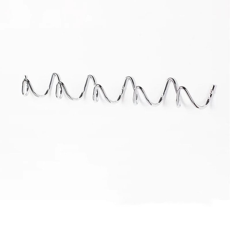 May include: A chrome-finished metal wall hook with a wavy design. The hook has multiple curved sections, creating several hanging points. The design is modern and minimalist, suitable for various spaces.
