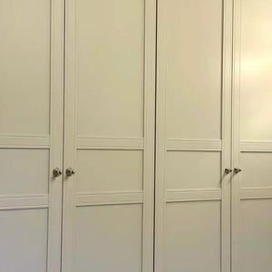 Puede incluir: Un conjunto de cuatro puertas de armario de color beige claro con un dise&ntilde;o cl&aacute;sico de estilo shaker, que presenta paneles empotrados y rieles horizontales. Cada puerta cuenta con un peque&ntilde;o pomo redondo de metal plateado.