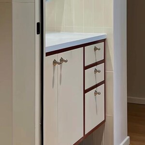 Puede incluir: Un mueble de cocina con puertas y frentes de caj&oacute;n en color blanco roto, enmarcados por un borde de madera oscura. La unidad incluye una puerta de armario grande y tres cajones apilados, con peque&ntilde;os pomos c&oacute;nicos plateados.