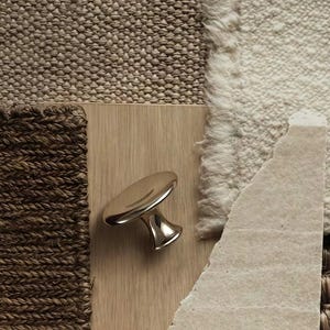 Puede incluir: Un pomo de mueble met&aacute;lico pulido con una parte superior circular lisa y una base c&oacute;nica, montado sobre una superficie de madera clara. El pomo presenta un acabado plateado reflectante que capta la luz, resaltando su forma curva.