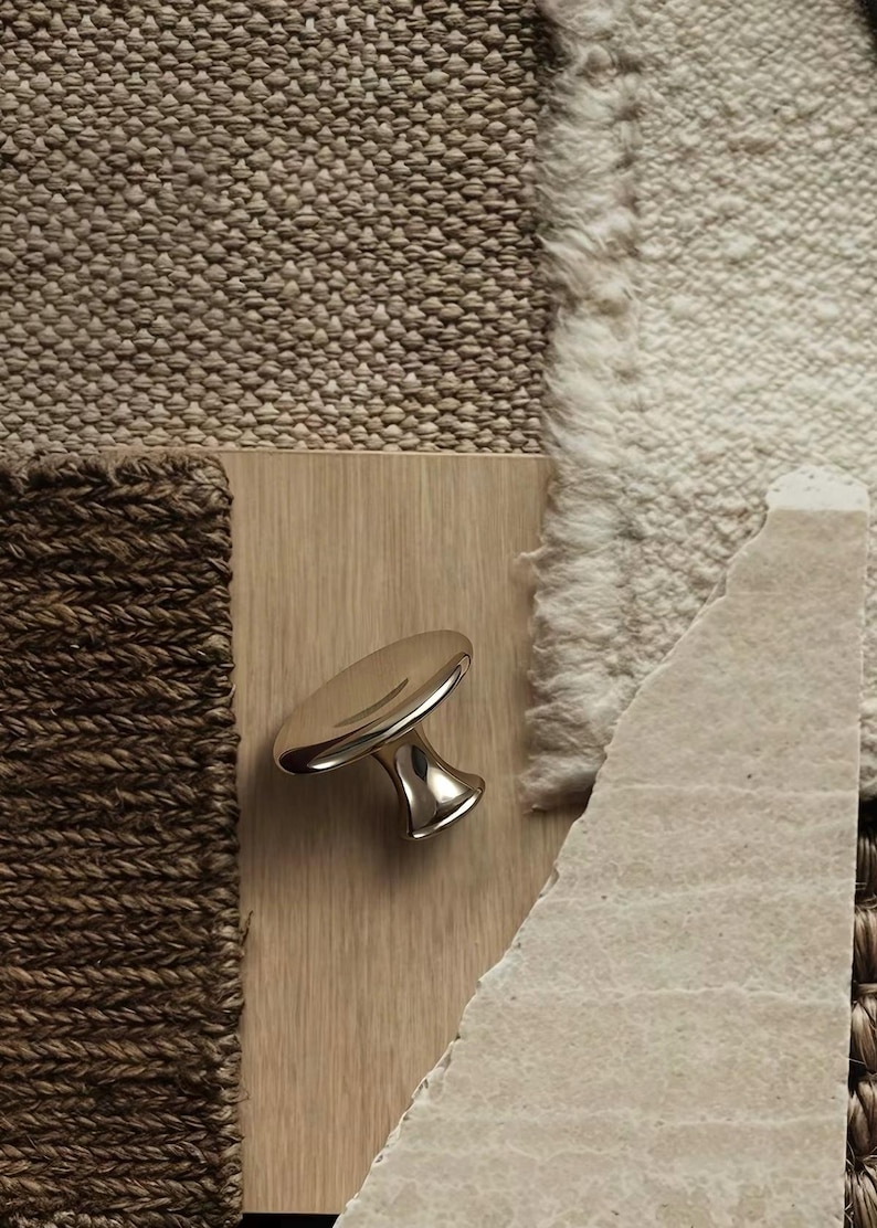Puede incluir: Un pomo de mueble met&aacute;lico pulido con una parte superior circular lisa y una base c&oacute;nica, montado sobre una superficie de madera clara. El pomo presenta un acabado plateado reflectante que capta la luz, resaltando su forma curva.