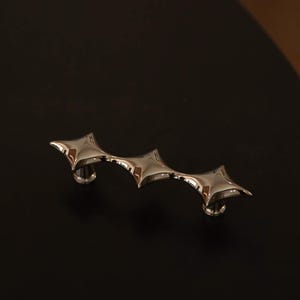 May include: A polished silver-tone metal cabinet pull featuring a continuous, elongated design with three distinct, four-pointed star-shaped sections connected in a row. The hardware has a reflective, smooth surface and two circular mounting bases.