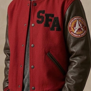 May include: A red wool varsity jacket with brown leather sleeves. The jacket features the letters "SFA" in black on the chest and a circular patch on the sleeve. Black and brown striped cuffs and collar complete the look.