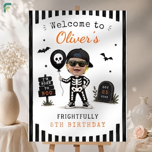 Puede incluir: Un cartel de cumpleaños rectangular con rayas verticales blancas y negras en los bordes. El texto dice Welcome to Oliver's, I BORN TO BOO, OCT 25 2026 y FRIGHTFULLY 5TH BIRTHDAY. Incluye un personaje esqueleto con una cara de fotografía.