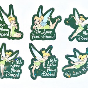May include: Six die-cut stickers featuring the character Tinker Bell in various poses. Each sticker has a dark green background with the white text "We Love Your Door!" and small colorful star accents. The character has blonde hair and wings.