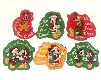 May include: Six die-cut stickers featuring Disney characters in holiday attire. Each sticker displays the text "We Love Your Door!" and depicts Pluto, Minnie Mouse, or Mickey Mouse in festive scenes with candy canes, Christmas lights, and Santa hats.