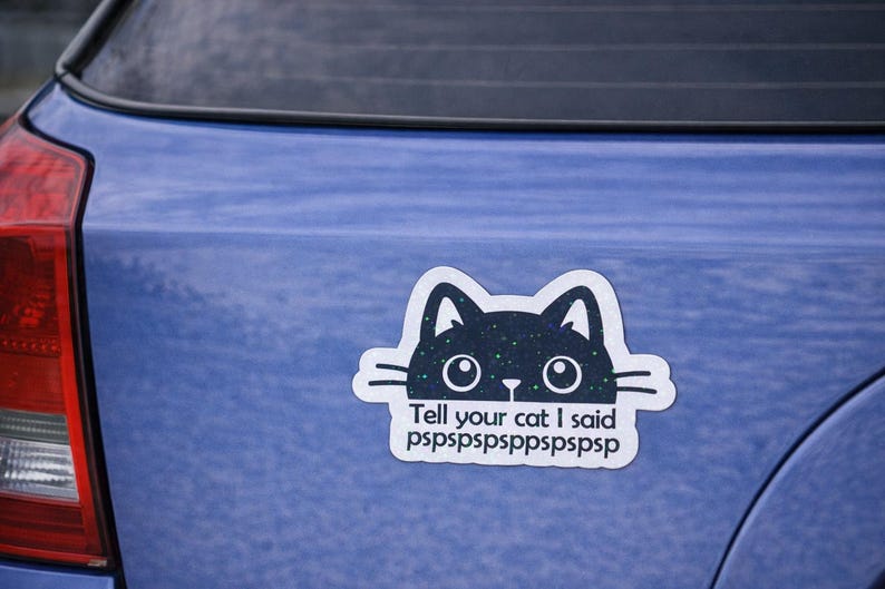 May include: A die-cut vinyl sticker featuring a dark blue cat head with a starry night pattern and large white eyes. Below the cat, the text reads: Tell your cat I said pspspspsppspspsps. The sticker is applied to the blue boot of a vehicle.