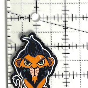 May include: A cartoon lion character with a black mane and orange fur, with an angry expression. The image is approximately 3.8 cm in height. The character is sitting down. The image has a colorful design.