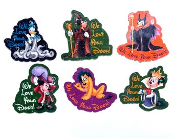 May include: A set of six die-cut stickers featuring Disney characters including Donald Duck, Goofy, Maleficent, Mickey Mouse, Pluto, and Minnie Mouse. Each sticker displays the text We Love Your Door! in a stylised font with colourful backgrounds.