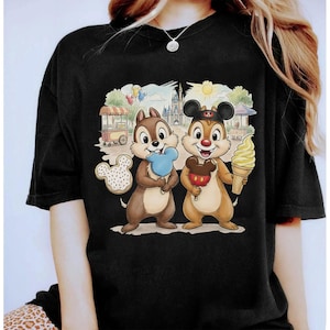 May include: Black t-shirt featuring a colorful graphic of two cartoon chipmunks holding ice cream cones and treats. The design includes a castle, food carts, and balloons, creating a fun, whimsical scene. The shirt is a comfortable, casual wear.