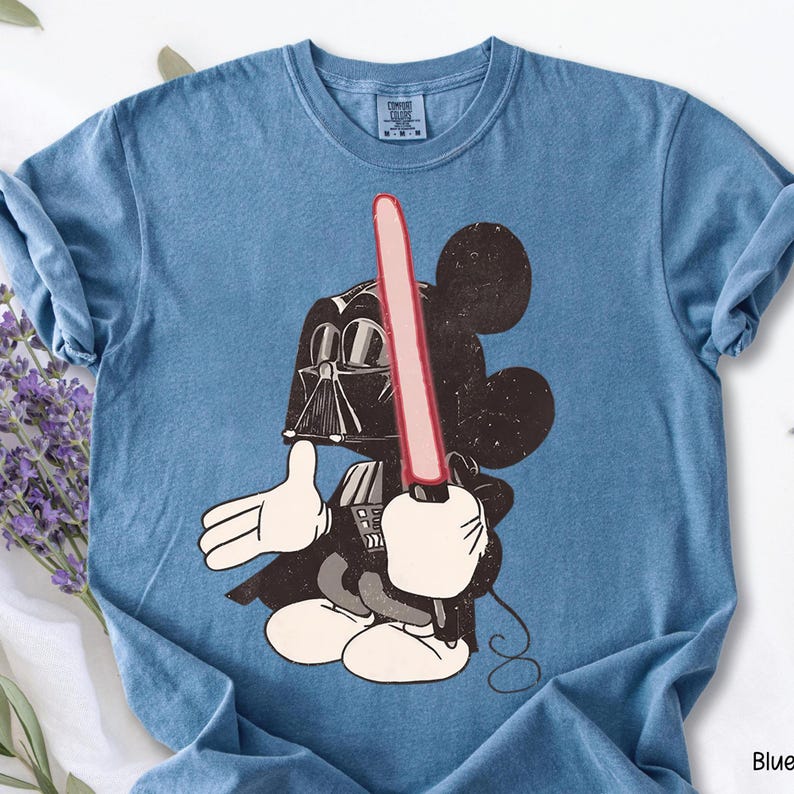 May include: Blue t-shirt featuring a cartoon character mashup of Mickey Mouse as Darth Vader, holding a red lightsaber. The graphic is distressed, giving a vintage look. The shirt has a crew neck and short sleeves.