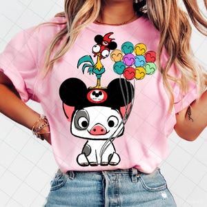 May include: Pink t-shirt featuring a cartoon illustration of a pig with Mickey Mouse ears, a rooster, and colorful balloons. The pig has a black and white body, and the rooster is blue, yellow, and red. The balloons are various colors.