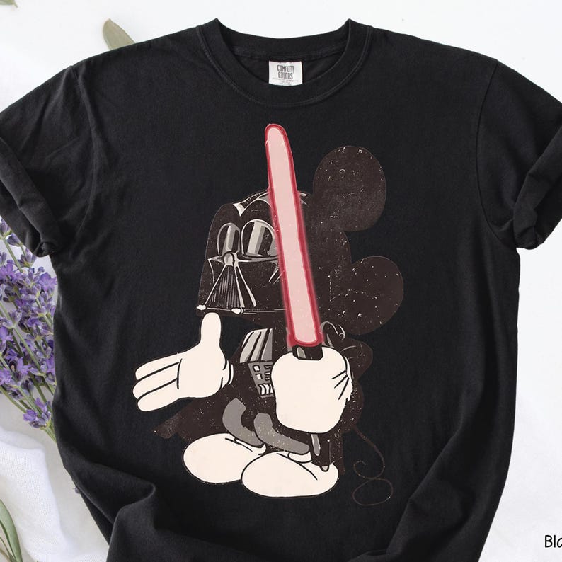May include: Black t-shirt featuring a graphic of Mickey Mouse as Darth Vader, holding a red lightsaber. The design includes Mickey's iconic ears and white gloves. The shirt is made of a soft material.