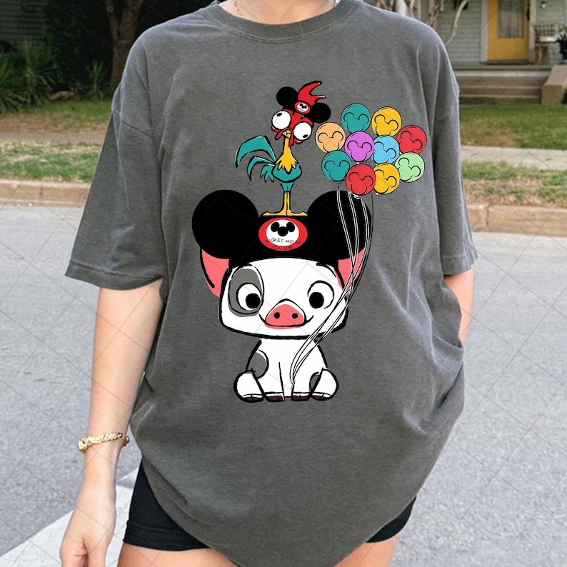 May include: Dark gray t-shirt featuring a cartoon pig character with Mickey Mouse ears, a rooster, and colorful balloons. The pig is white with black spots and a pink snout. The rooster is yellow, red, and blue.