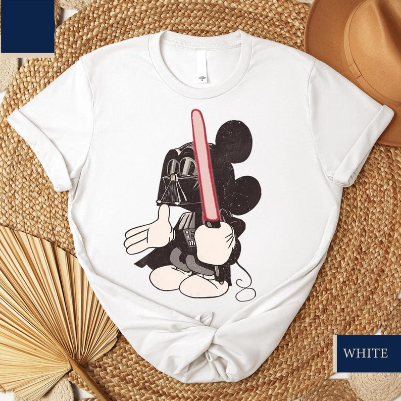 May include: White t-shirt featuring a cartoon Mickey Mouse character dressed as Darth Vader, holding a red lightsaber. The design is in black and white with red accents. The shirt is a crew neck.