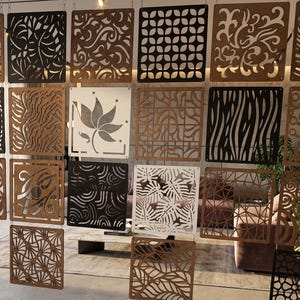 Puede incluir: Un separador de ambientes compuesto por múltiples paneles cuadrados suspendidos del techo. Los paneles presentan varios patrones cortados con láser, incluidos diseños florales, geométricos y abstractos, en tonos marrón, negro y blanco.