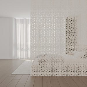 Könnte beinhalten: Eine weiße Glasblockwand mit Muster ist der Mittelpunkt dieser Innenaufnahme. Die Wand besteht aus quadratischen Blöcken mit einem sich wiederholenden floralen Design. Ein durchsichtiger weißer Vorhang und ein hellfarbiger Teppich sind ebenfalls zu sehen.
