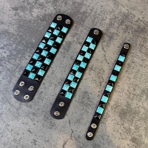 May include: Three black wristbands of varying widths, each featuring a grid of square turquoise studs. The wristbands are secured with silver-toned metal snap buttons at the ends, arranged in rows of two or one depending on the width.