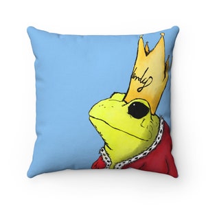 May include: A blue throw pillow with a cartoon illustration of a frog wearing a gold crown with the word "Wendy" written on it. The frog is wearing a red robe with a gold trim.