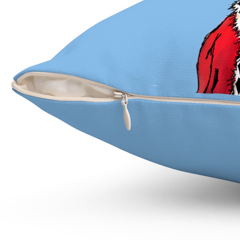 May include: A light blue throw pillow with a zipper closure. The pillow has a printed design of a cartoon character wearing a red and white outfit.