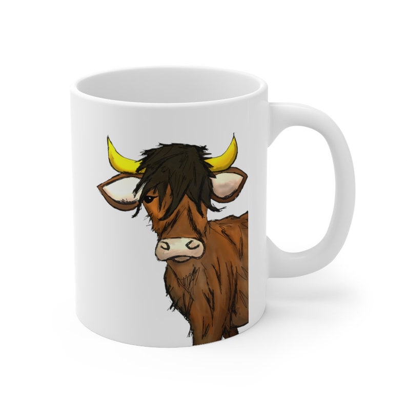 K&ouml;nnte beinhalten: Wei&szlig;e Keramiktasse mit einer Cartoon-Illustration einer braunen Kuh mit schwarzen Haaren und gelben H&ouml;rnern. Die Kuh ist in einem skurrilen Stil gezeichnet, mit einem seitlichen Blick. Die Tasse hat einen Standardgriff und ein gl&auml;nzendes Finish.