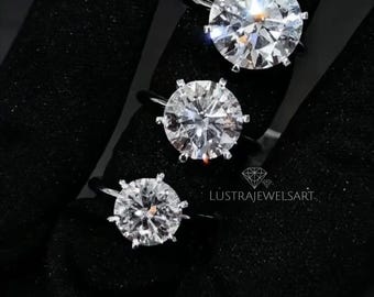 May include: Three silver-toned rings with round, brilliant-cut clear stones set in six-prong settings. The rings are arranged in a vertical line, with the largest at the top and smallest at the bottom. Text reads LUSTRAJEWELSART with a diamond icon.