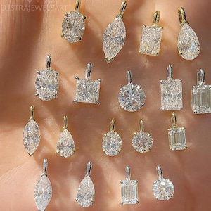 Può includere: Una collezione di pendenti con diamanti di varie forme, tra cui ovali, a goccia e taglio smeraldo. I pendenti sono incastonati in oro e argento, mettendo in risalto la brillantezza dei diamanti. Il testo "LUSTRAJEWELART" è presente.
