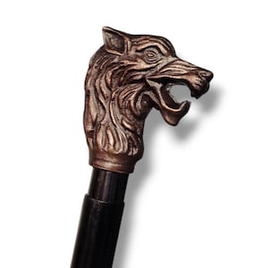 May include: A walking stick featuring a bronze wolf head handle. The wolf head is highly detailed with an open mouth and sharp teeth. The shaft of the stick is black. A decorative accessory.