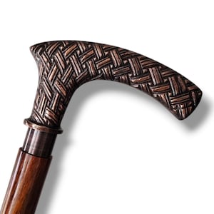 Puede incluir: Bastón de madera con empuñadura curva. El mango presenta un diseño tejido en tonos bronce y marrón. El eje es de madera pulida de color marrón oscuro. Una ayuda a la movilidad decorativa y funcional.