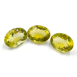 Könnte beinhalten: Drei oval geschliffene, facettierte Edelsteine mit einem blassgelben Farbton werden vor einem weißen Hintergrund präsentiert. Die Edelsteine haben eine polierte, reflektierende Oberfläche, die ihre innere Struktur und Klarheit hervorhebt. Die Anordnung deutet auf eine Sammlung loser Edelsteine hin.
