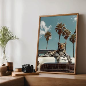 K&ouml;nnte beinhalten: Gerahmter Kunstdruck mit einem Leoparden, der auf einem wei&szlig;en Oldtimer liegt. Der Hintergrund zeigt Palmen unter blauem Himmel mit Wolken. Das Kunstwerk hat ein Retro-Tropen-Thema.
