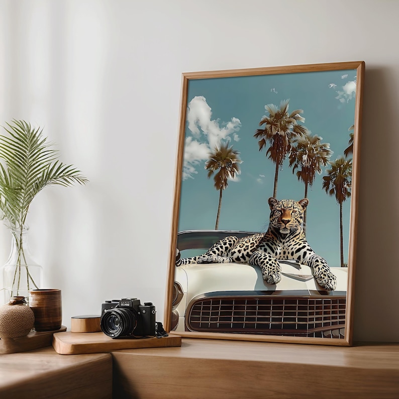 K&ouml;nnte beinhalten: Gerahmter Kunstdruck mit einem Leoparden, der auf einem wei&szlig;en Oldtimer liegt. Der Hintergrund zeigt Palmen unter blauem Himmel mit Wolken. Das Kunstwerk hat ein Retro-Tropen-Thema.