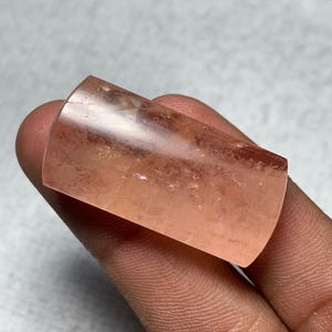 May include: A translucent, peach-colored crystal with a cylindrical shape. The crystal has a smooth, polished surface and appears to be a gemstone or mineral specimen. The light passes through the crystal, highlighting its internal structure.