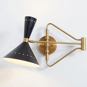 Può includere: Applique da parete nero e oro con paralume a forma di cono e braccio in ottone. L'applique ha un design moderno della metà del secolo, con paralume nero e braccio color oro. Il paralume ha piccoli fori.
