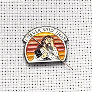 Könnte beinhalten: Metall-Anstecknadel mit dem Schriftzug "I NEVER SAID THAT" und einer Illustration einer Person, die sich das Gesicht verdeckt. Der Hintergrund ist ein Sonnenuntergang in Orange, Rot und Gelb.