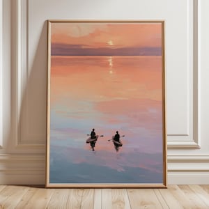 Könnte beinhalten: Ein gerahmter Wandkunstdruck, der einen ruhigen Sonnenuntergang über einem stillen Gewässer zeigt. Zwei Personen sind als Silhouetten auf separaten Kajaks zu sehen, wie sie über die spiegelnde Oberfläche in sanften Pfirsich-, Rosa- und Blautönen gleiten.
