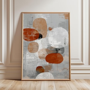 May include: Abstract art print with overlapping shapes in orange, grey, white, and black. The artwork is framed in natural wood and leans against a white wall and wooden floor. The shapes vary in size and texture, creating a modern aesthetic.