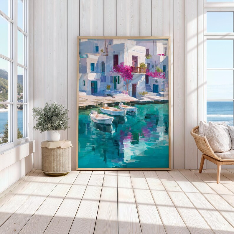 May include: A framed art print depicts a coastal scene with white buildings, blue doors, and pink flowers. Three small boats float on turquoise water. The artwork is displayed in a bright room with a window overlooking the ocean.