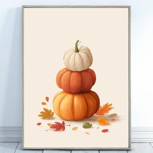 Könnte beinhalten: Ein vertikaler Wandkunstdruck mit einem Stapel aus drei Kürbissen in den Farben Creme, Orange und Dunkelorange. Die Kürbisse sind vertikal angeordnet und von verstreuten Herbstblättern in Rot-, Gelb- und Grüntönen umgeben.