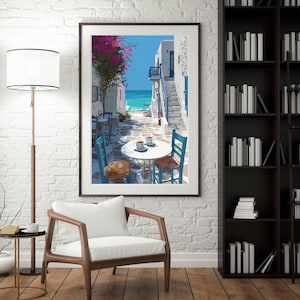 May include: Framed art print depicting a coastal scene with white buildings, blue accents, and a turquoise sea. A table with two cups of coffee and chairs are in the foreground. Pink flowers and a blue sky complete the scene.